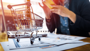 A imagem ilustra o conceito de e-commerce e vendas digitais, destacando elementos de compras e análises financeiras em uma mesa de trabalho.