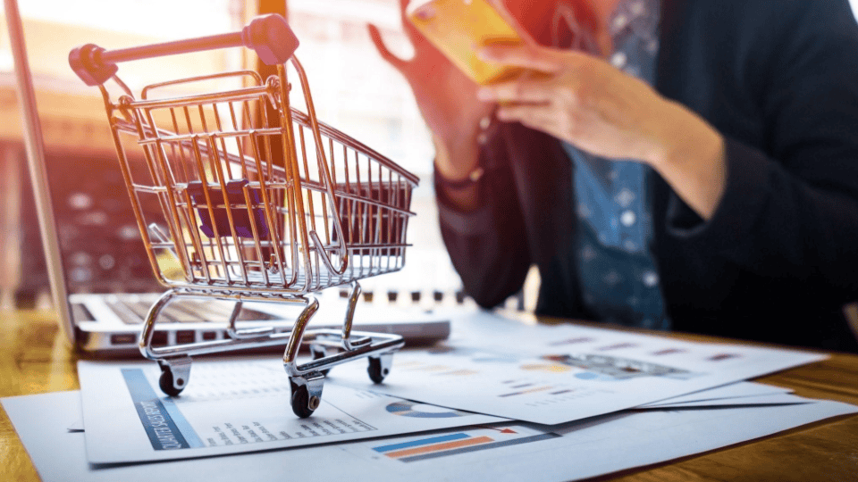 A imagem ilustra o conceito de e-commerce e vendas digitais, destacando elementos de compras e análises financeiras em uma mesa de trabalho.